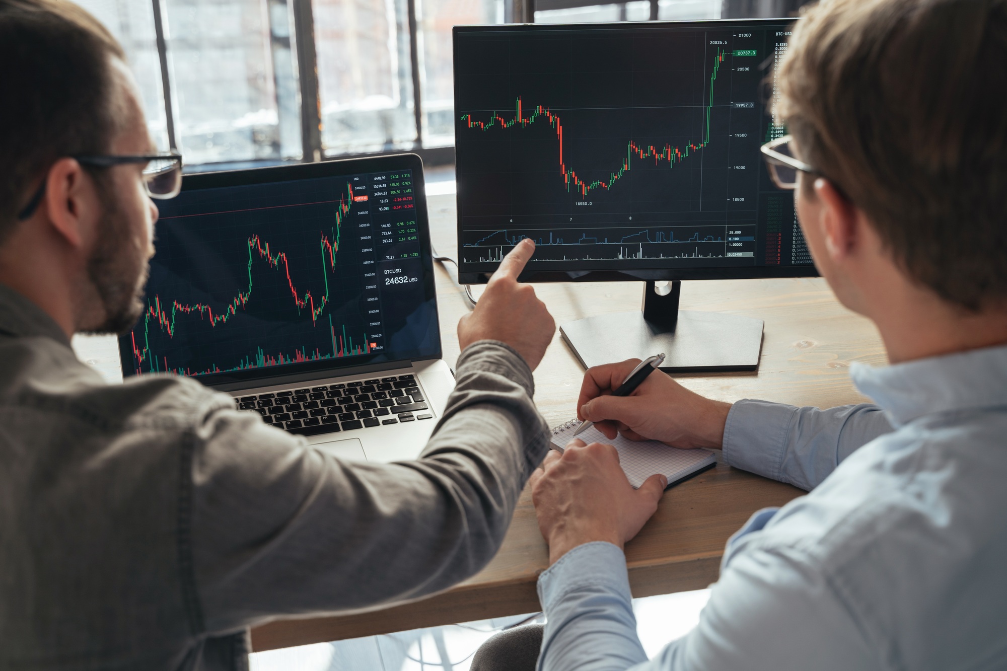 crypto traders sitting together in front of PCs, monitoring candlestick charts